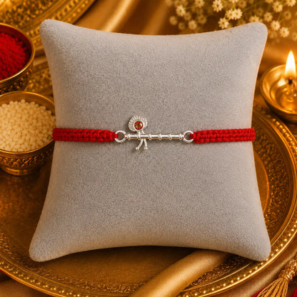 Silver Basuri Rakhi with red mauli thread on a white cushion with golden festive background
