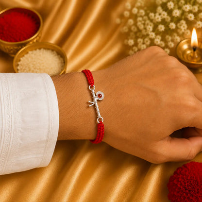 Silver Basuri Rakhi with red mauli thread on a white cushion with golden festive background