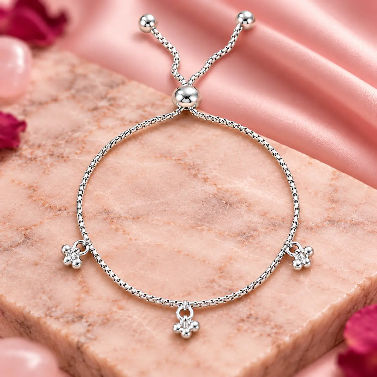 Silver beaded charm bracelet for women with adjustable slider clasp and dangling ball charms on a beige background
