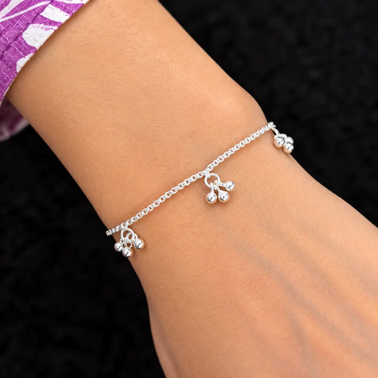 Silver beaded charm bracelet for women with adjustable slider clasp and dangling ball charms on a beige background