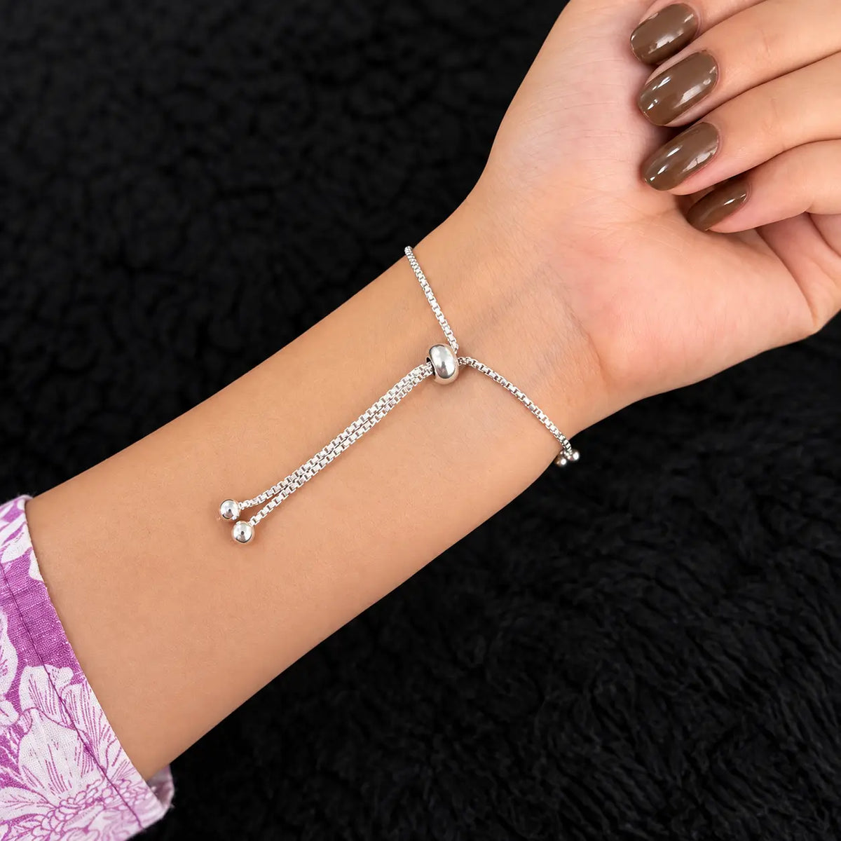 Silver beaded charm bracelet for women with adjustable slider clasp and dangling ball charms on a beige background