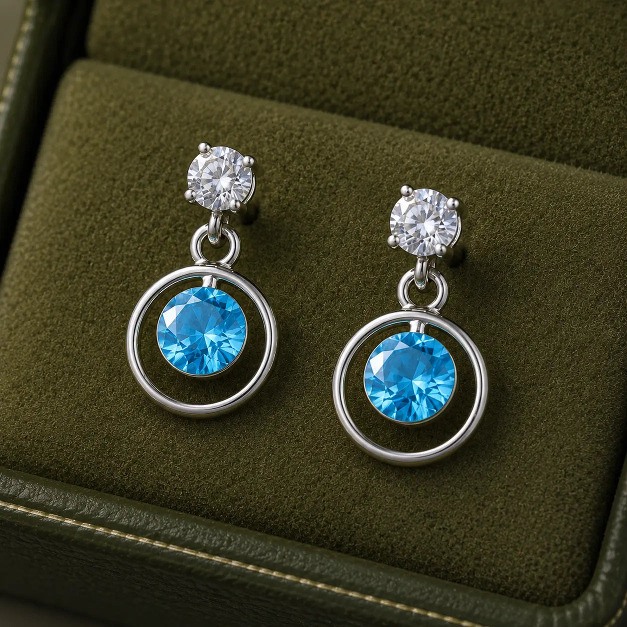 Silver blue round cubic zirconia open circle drop earrings for women with polished silver finish and sparkling crystal accents displayed on a white rose branch.