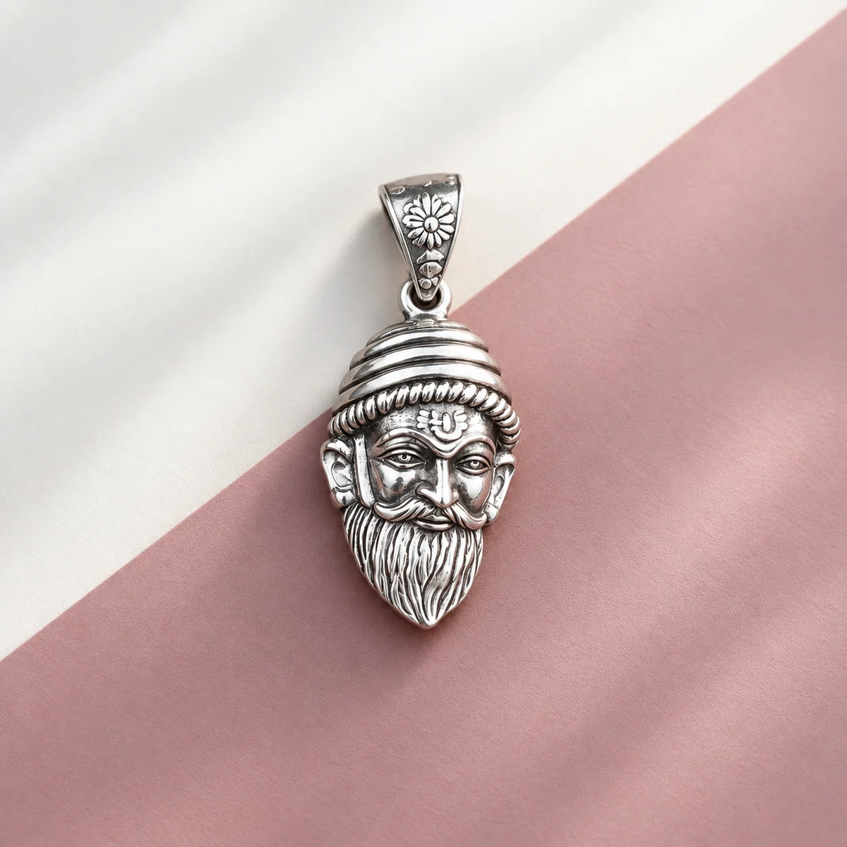 Silver Chhatrapati Shivaji Maharaj face pendant with detailed royal headgear, moustache, and beard on a white and dusty pink background