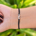 Silver infinity bracelet with black thread worn on wrist