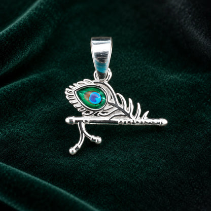 Silver Krishna flute peacock feather pendant with blue and green enamel detailing on a dark teal velvet background