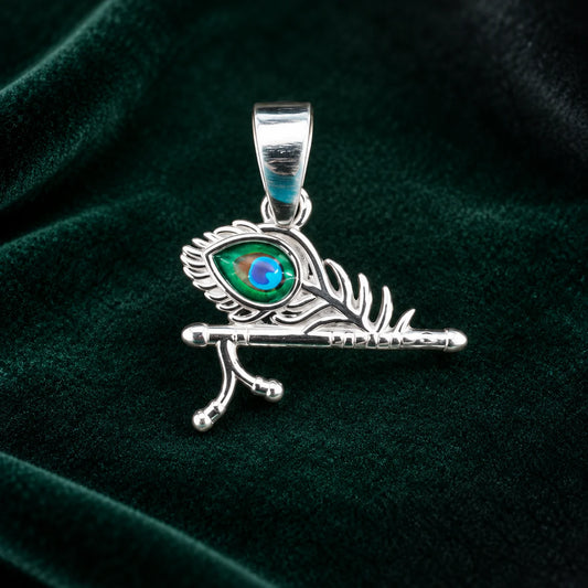 Silver Krishna flute peacock feather pendant with blue and green enamel detailing on a dark teal velvet background