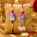  Silver Om Floral Rakhi Set with Pearl Lumba Rakhi for Bhai and Bhabhi featuring handcrafted pink blue flowers, pearl beads, and red thread for Raksha Bandhan.