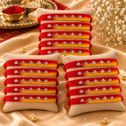 "Set of 15 handcrafted red and yellow thread Rakhis with silver Om charms displayed on a beige velvet cushion, perfect for Raksha Bandhan celebrations."