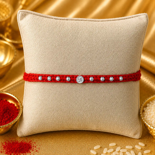 Silver Swastik Rakhi with red braided thread and silver beads on a festive cream cushion