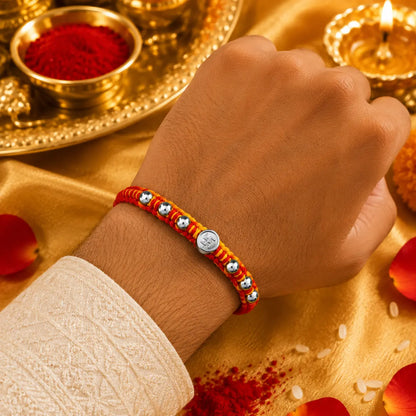 Premium silver Swastik Rakhi with red and yellow thread and silver beads on a beige cushion