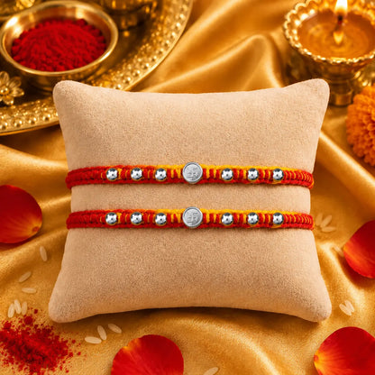 Premium silver Swastik Rakhi with red and yellow thread and silver beads on a beige cushion