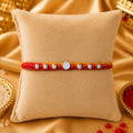 Premium silver Swastik Rakhi with red and yellow thread and silver beads on a beige cushion