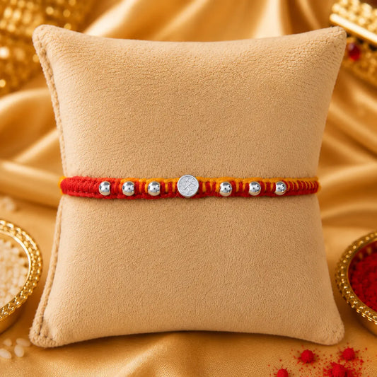 Premium silver Swastik Rakhi with red and yellow thread and silver beads on a beige cushion