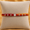 Premium silver Swastik Rakhi with red and yellow thread and silver beads on a beige cushion