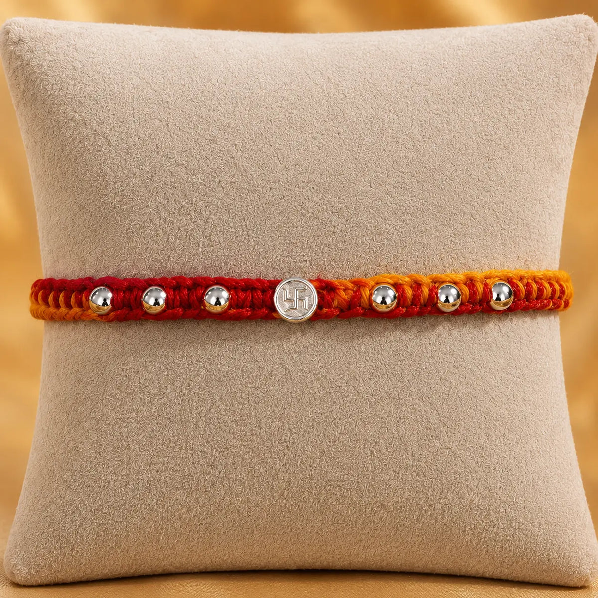 Premium silver Swastik Rakhi with red and yellow thread and silver beads on a beige cushion