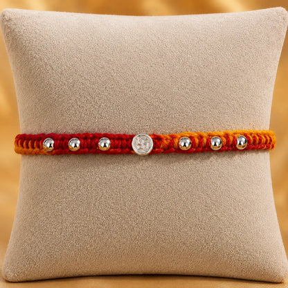 Premium silver Swastik Rakhi with red and yellow thread and silver beads on a beige cushion