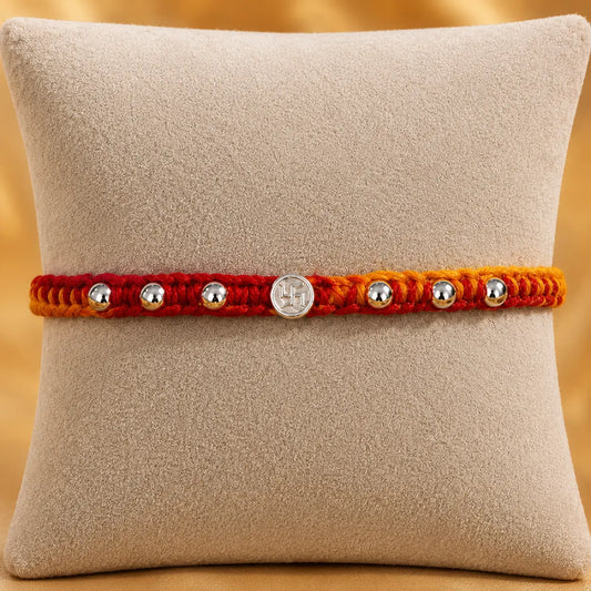 Premium silver Swastik Rakhi with red and yellow thread and silver beads on a beige cushion