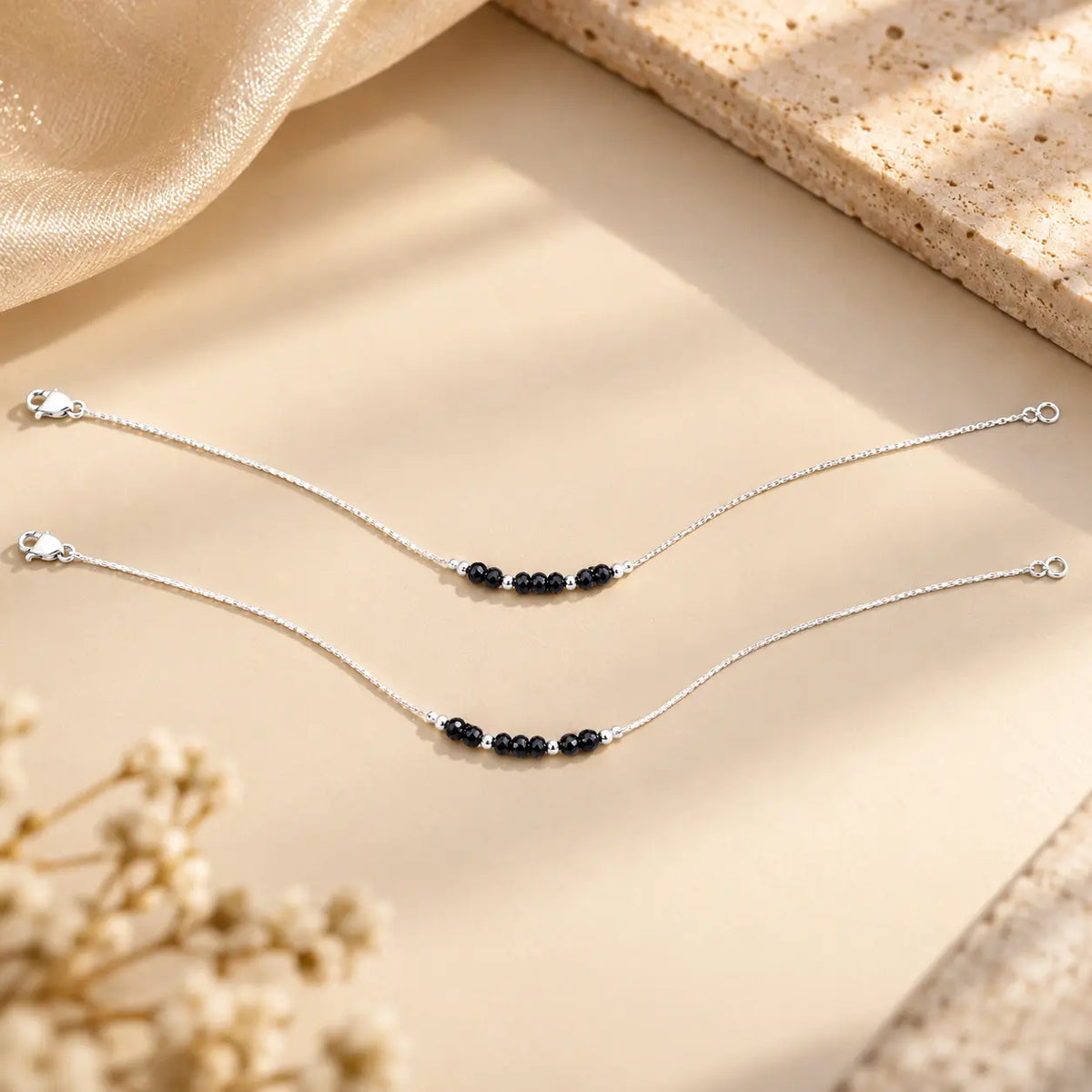 Silver anklet pair with black beads on a beige background by Khushbu Jewellers
