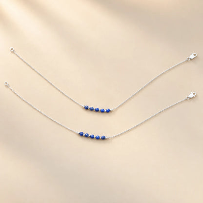 Silver anklet pair with blue beads and silver spacers on a beige background by Khushbu Jewellers