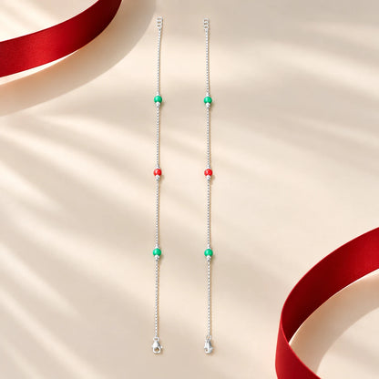 Silver anklet pair with red and green beads on a cream background by Khushbu Jewellers