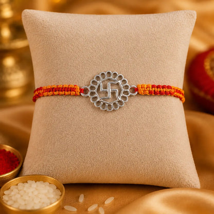925 Sterling Silver Swastik Rakhi displayed on a premium beige cushion with festive Raksha Bandhan decor including kumkum, rice, marigold flowers, brass pooja thali, and diya.