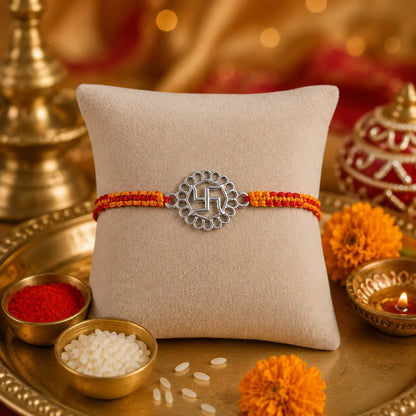 925 Sterling Silver Swastik Rakhi displayed on a premium beige cushion with festive Raksha Bandhan decor including kumkum, rice, marigold flowers, brass pooja thali, and diya.