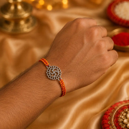 925 Sterling Silver Swastik Rakhi displayed on a premium beige cushion with festive Raksha Bandhan decor including kumkum, rice, marigold flowers, brass pooja thali, and diya.
