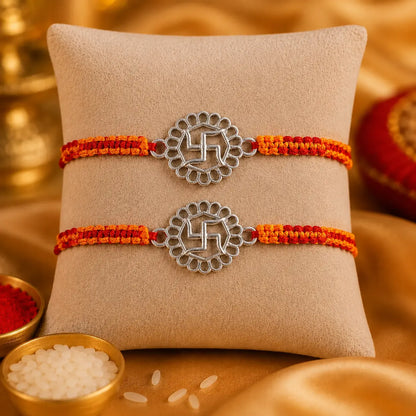 925 Sterling Silver Swastik Rakhi displayed on a premium beige cushion with festive Raksha Bandhan decor including kumkum, rice, marigold flowers, brass pooja thali, and diya.