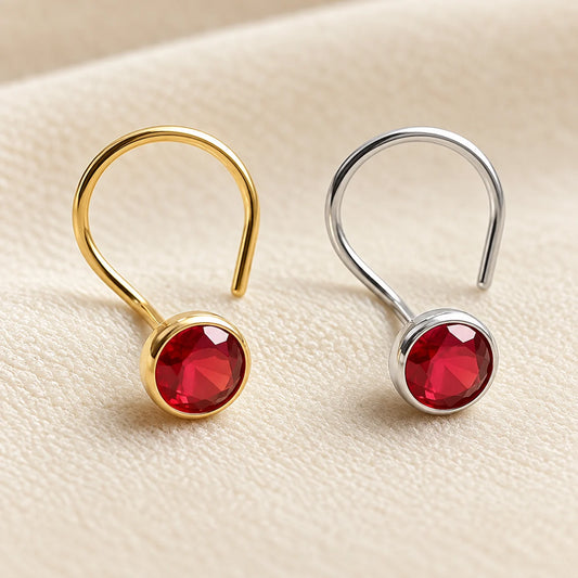Two small hoop-style earrings with round faceted red gemstones, one in gold-tone metal and one in silver-tone metal, displayed on a light beige textured surface.