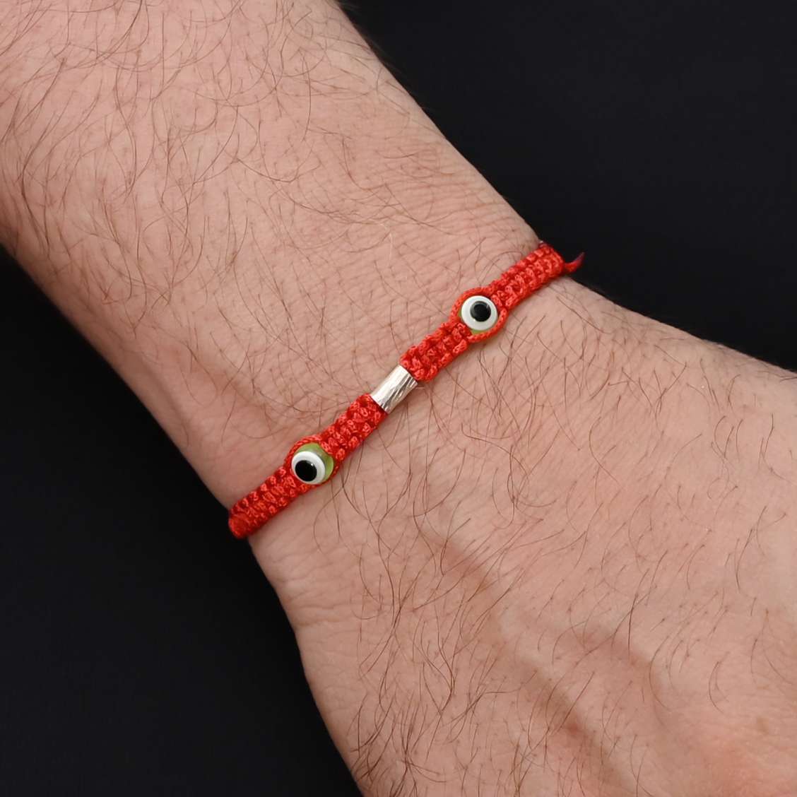 Elegant Rakhi with two green evil eyes in silver, ideal for boys.