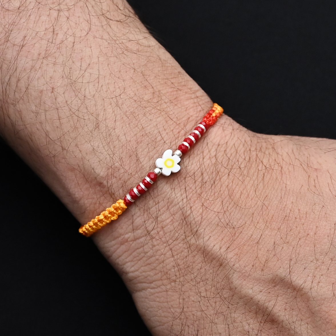 Elegant Rakhi with a white flower centerpiece and silver and light red beads, ideal for boys.