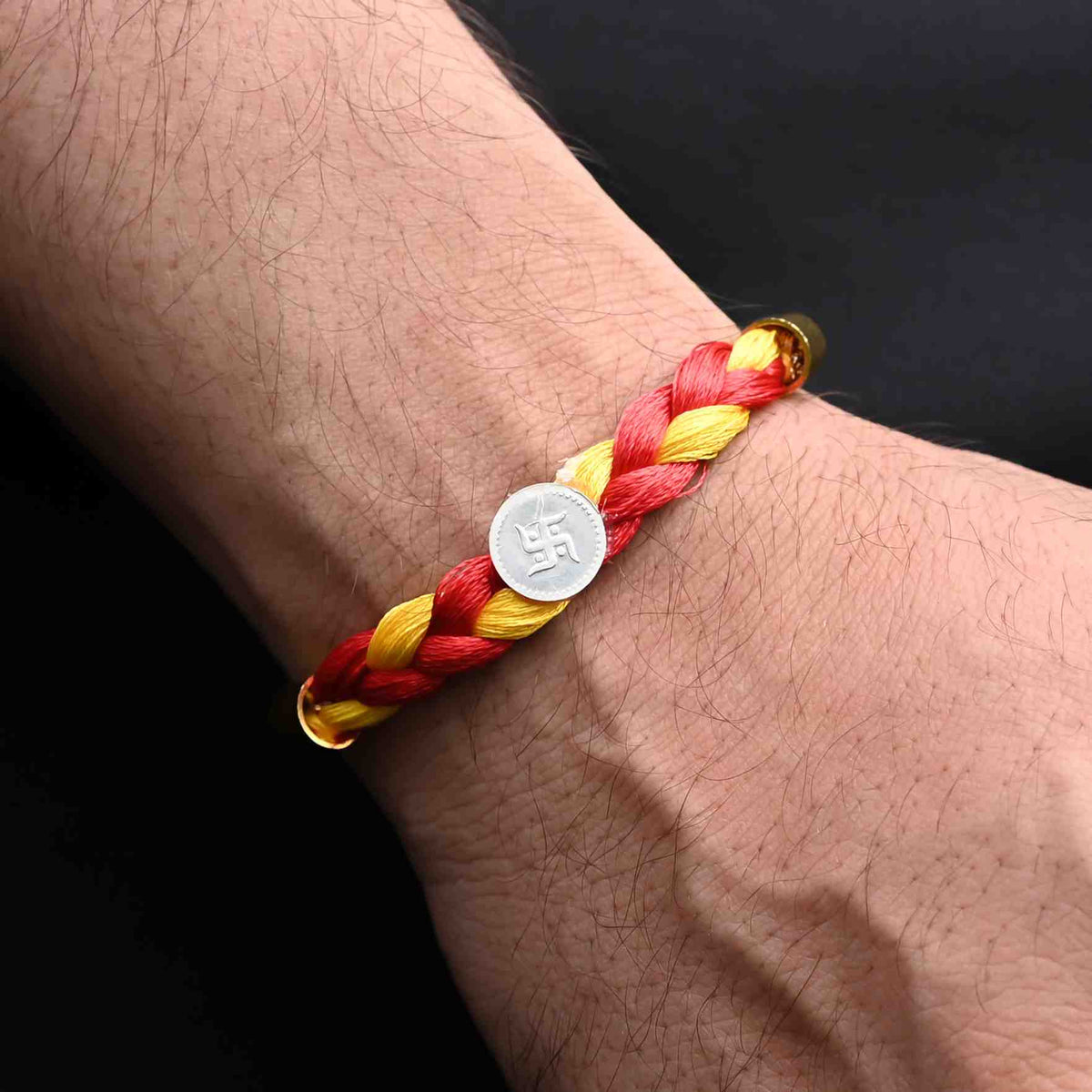 Elegant Rakhi with a silver Swashtika symbol and vibrant red and yellow tangle Moli, ideal for boys