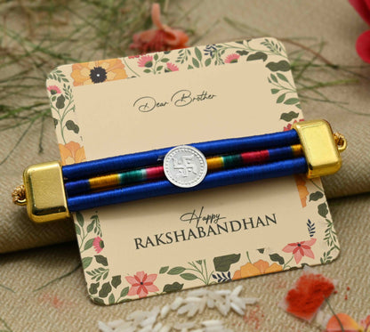 Silver center Swashtika design with a blue ribbon, perfect Rakhi for boys.