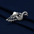 A silver-toned peacock brooch with clear gemstones and a small red eye accent, displayed on a textured dark navy blue fabric background.
